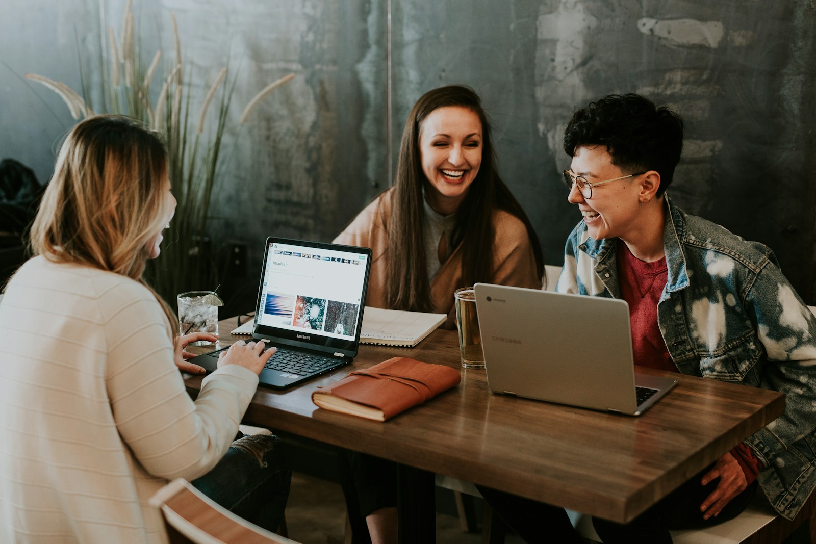 Three students laughing and comparing colleges together on their laptops
