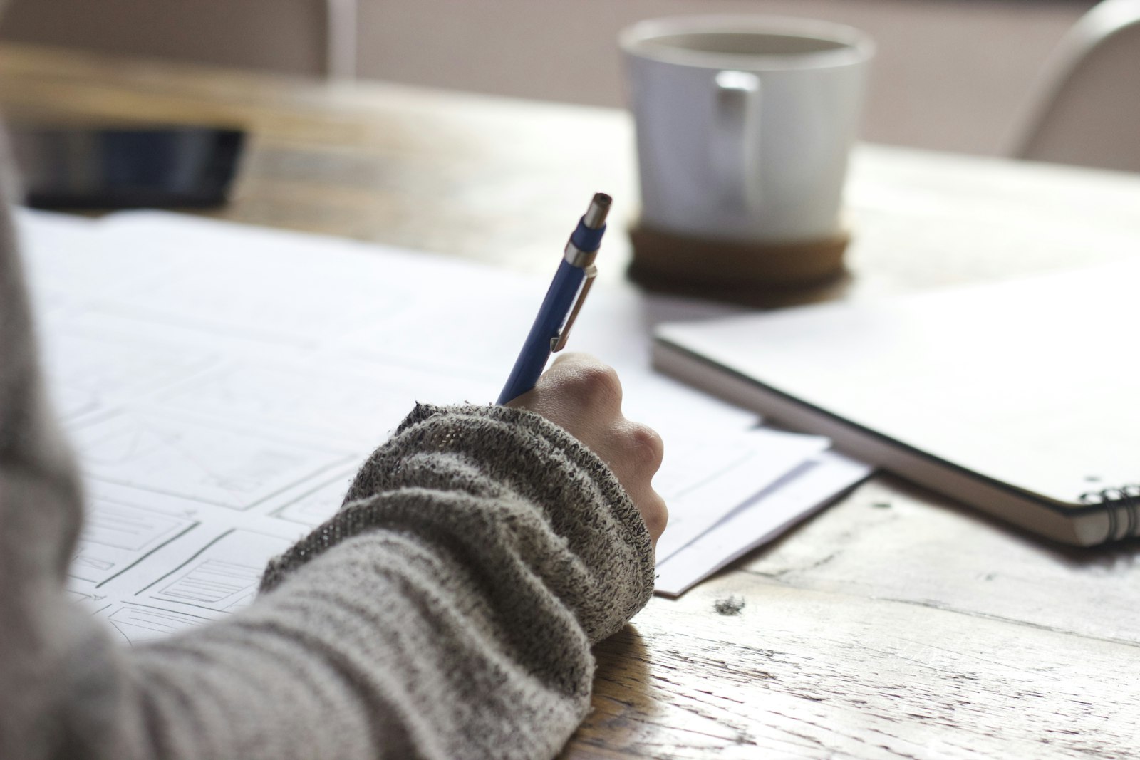 Student taking notes at a desk next to a laptop and a cup of coffee